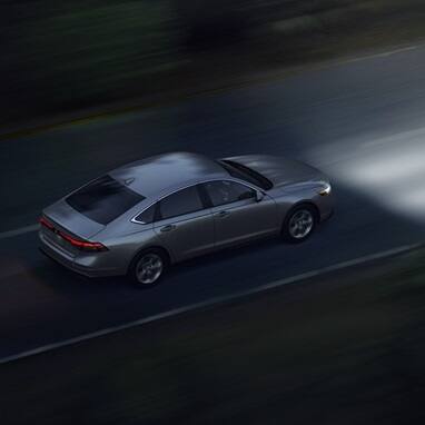 High angled 3/4 rear passenger shot of the 2026 Honda Accord driving on an open road at night.