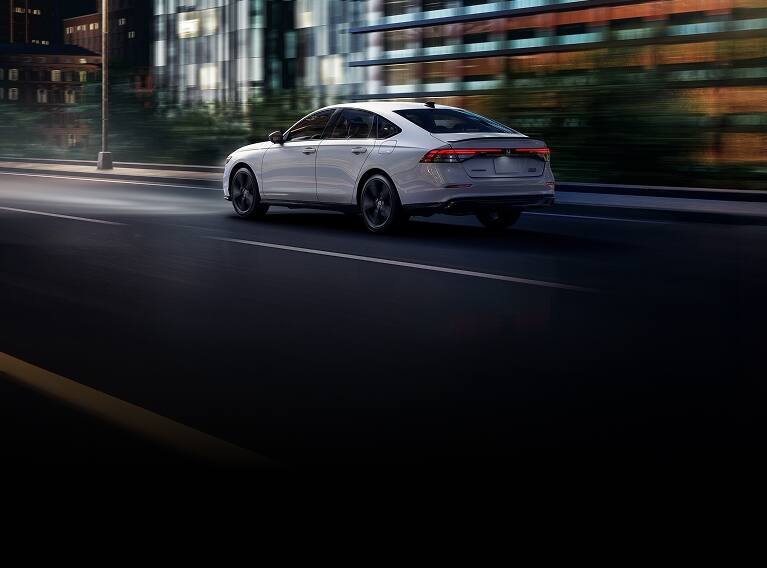 2026 Honda Accord 3/4 rear view in Platinum White Pearl driving in the city at night.