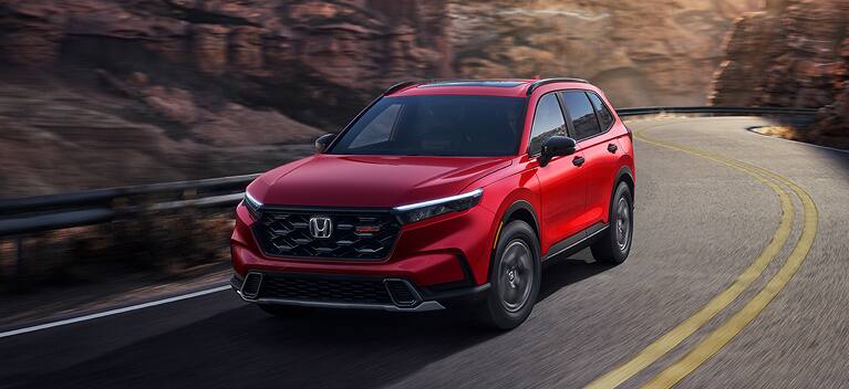 2027 Honda CR-V TrailSport Hybrid in Radiant Red Metallic front driving on a winding mountain road (Compact Crossover SUV).